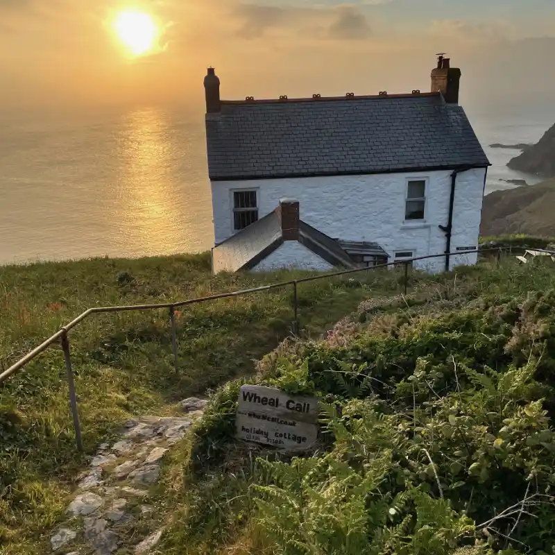 Wheal Call holiday cottage at sunset with steps in foreground and sign showing contact and booking details